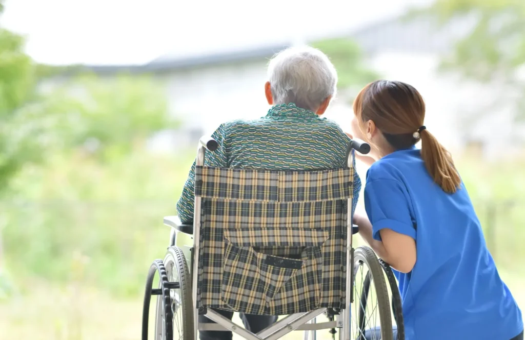 Pflegerin begleitet einen Senior im Rollstuhl im Garten